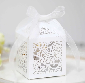 Close-up of laser-cut white wedding favor box with floral patterns and a silk ribbon bow