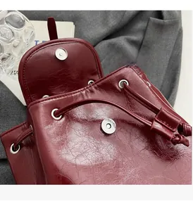 Detail of burgundy waxed leather backpack featuring drawstring and silver magnetic closure