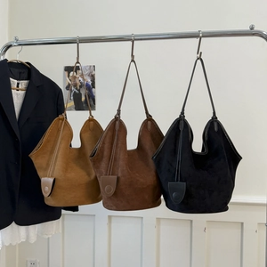 Close-up of three suede hobo tote bags in khaki, brown, and black colors on display