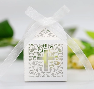 Close-up of white laser-cut wedding favor box with cross design and organza ribbon