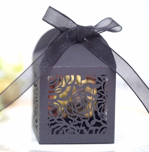 Detail of hollow laser-cut rose patterns on black wedding favor box with ribbon