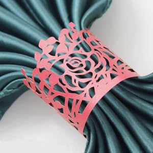 Close-up of coral red laser-cut rose napkin ring on a dark green satin cloth