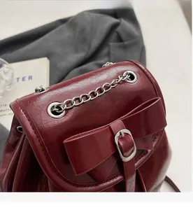Detail of burgundy glossy leather backpack with bow accent and silver metal chain