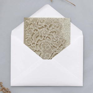 Macro shot of laser-cut lace floral pattern on champagne gold glitter wedding invitation