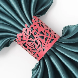 Close-up of laser-cut red rose paper napkin ring on dark green satin fabric