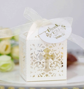 Close-up of white laser-cut wedding favor box with floral cross and thank you tag