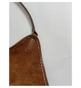 Detail of reinforced brown shoulder strap and fine stitching on a suede tote bag