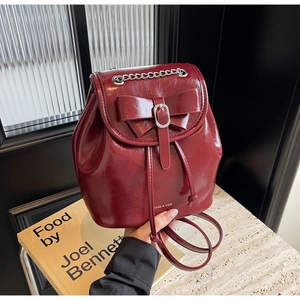 Close-up of wine red glossy leather backpack featuring a bow detail and silver metal hardware