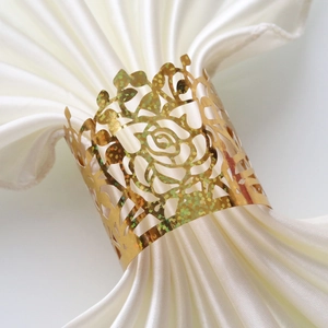 Close-up of golden rose hollow napkin ring on white satin fabric for wedding table decor