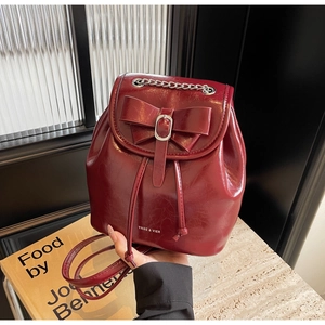Detail of burgundy patent leather backpack featuring a large bow and silver chain strap