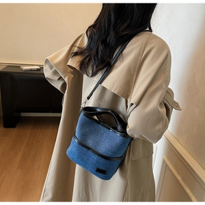 Detailed shot of the blue denim bucket bag with black leather trim and top handle