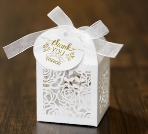 Detail of laser cut rose pattern on white wedding favor box with thank you tag and ribbon