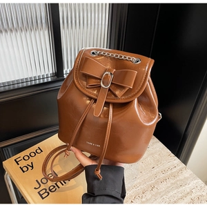Detail of vintage brown leather backpack with bow accent and chain on textured background