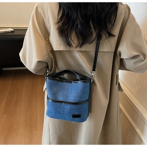 Rear view of model wearing a denim bucket bag with black leather straps and silver hardware