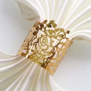 Detailed close-up of golden laser-cut rose napkin ring with glitter on white fabric