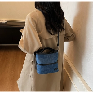 Detail of blue denim bucket bag with leather trim worn by model in a modern room