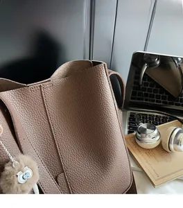 Detailed macro view of brown pebbled leather texture and plush owl charm on a tote bag