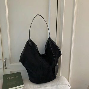 Detail of black suede tote bag with wing design and small leather pendant accessory