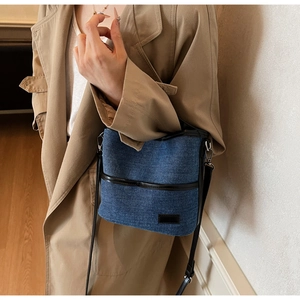Detail of blue denim bucket bag with black leather trim worn on a camel trench coat