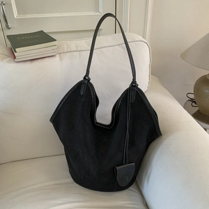Detail of a black suede tote bag with slim shoulder straps on a cozy white sofa