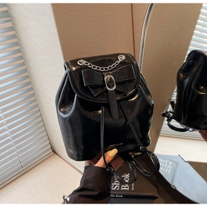 Detail of glossy black patent leather backpack with large bow and silver chain detail
