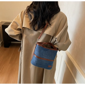 Detail of blue denim bucket bag with brown leather trim worn with a beige trench coat