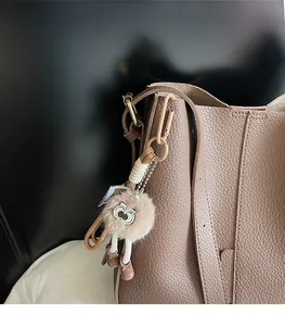 Close-up of fuzzy monster bag charm with large eyes on brown pebbled leather bucket bag