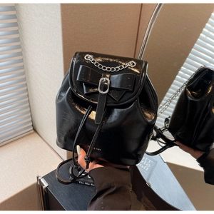 Detail of black patent leather mini backpack with silver chain and bow decoration