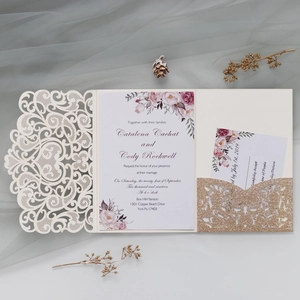 Detail of laser-cut cream wedding invitation with floral insert and glittery gold pocket
