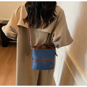 Detail of denim bucket bag with brown leather trim worn over a classic beige trench coat