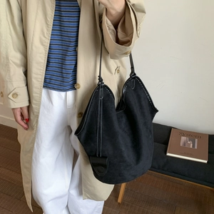 Detail of minimalist black suede tote bag with slim shoulder straps on a fashion model