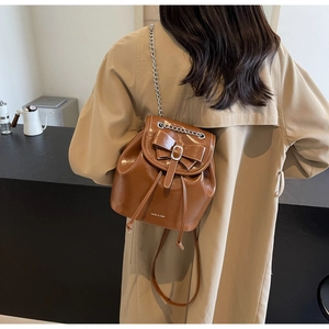 Brown glossy leather backpack detail with bow ornament and silver chain straps