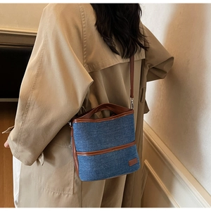 Detail of a denim bucket bag with brown leather straps worn with a beige trench coat