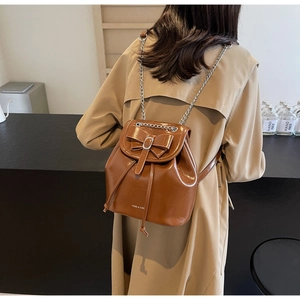 Detail of vintage caramel leather backpack with bow and metal chain strap on khaki trench coat