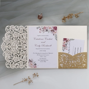 Detail view of laser-cut ivory wedding invitation with floral insert and gold glitter pocket