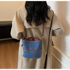 Blue denim bucket bag with brown leather accents worn by a model in a beige trench coat