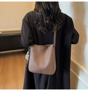 Retro brown bucket bag on model's shoulder with plush pendant detail for casual wear