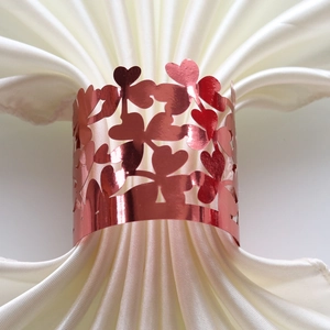 Dettaglio del portatovagliolo oro rosa con cuore traforato su tovagliolo di raso bianco