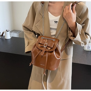 Detail of brown leather mini backpack featuring a decorative bow and silver chain strap