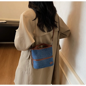 Detail showing denim bucket bag with brown leather trim worn with a beige trench coat