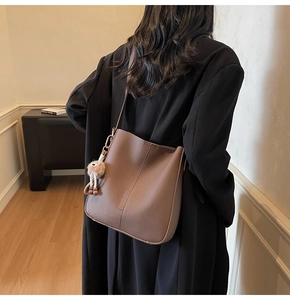 Detail view of brown pebbled leather bucket bag with plush charm and gold hardware