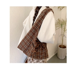 Detail of a brown plaid canvas tote bag with side strap and brand label on a model