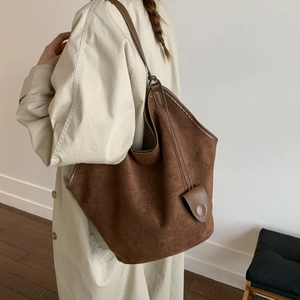 Detailed macro view of brown suede tote bag with slim shoulder straps and round charm