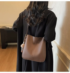 Detailed view of coffee brown litchi leather bucket bag with fuzzy ball charm on black coat