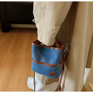 Detail of denim bucket bag showing brown leather trim and adjustable shoulder strap