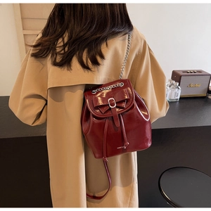 Detail of a dark red glossy backpack with a large bow and silver chain on a beige coat