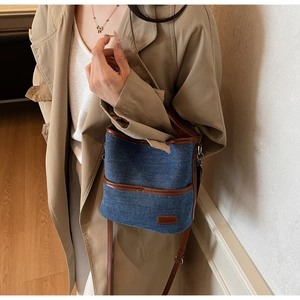 Close-up of denim and leather bucket bag showing stitching details and brown strap
