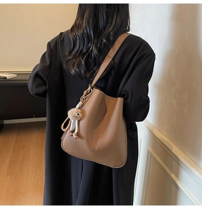 Detail of brown litchi pattern bucket bag with plush charm on a female model