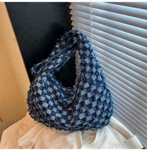 Detail of blue denim checkerboard tote bag with frayed edges on white clothing