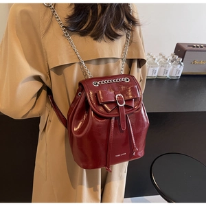Detail of burgundy patent leather backpack featuring a bow decoration and silver buckle